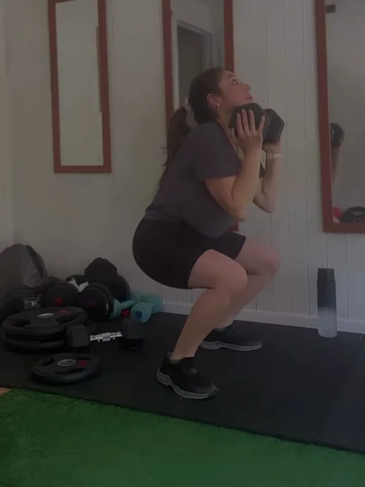 Alumna haciendo una sentadilla con mancuerna en la sala de entrenamiento